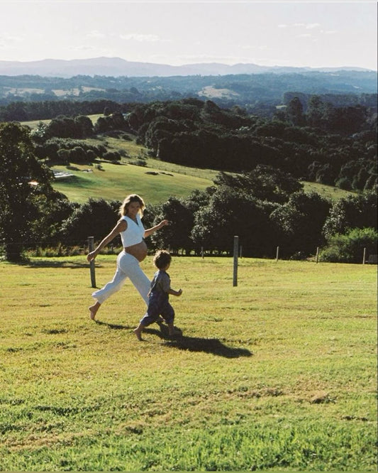  Pregnant woman running barefoot with a child on a grassy field, embracing ancestral wellness and supporting her pregnancy with beef organ supplements.